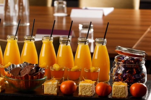 Selection of cakes, sweets and small bottles of orange juice lined up for a meeting at Mercure Hotels