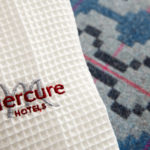 Close up of monogrammed Mercure Hotels dressing gown laid on a blue bedspread