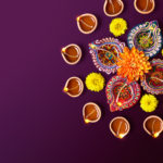 Colorful clay diya lamps with flowers on purple background